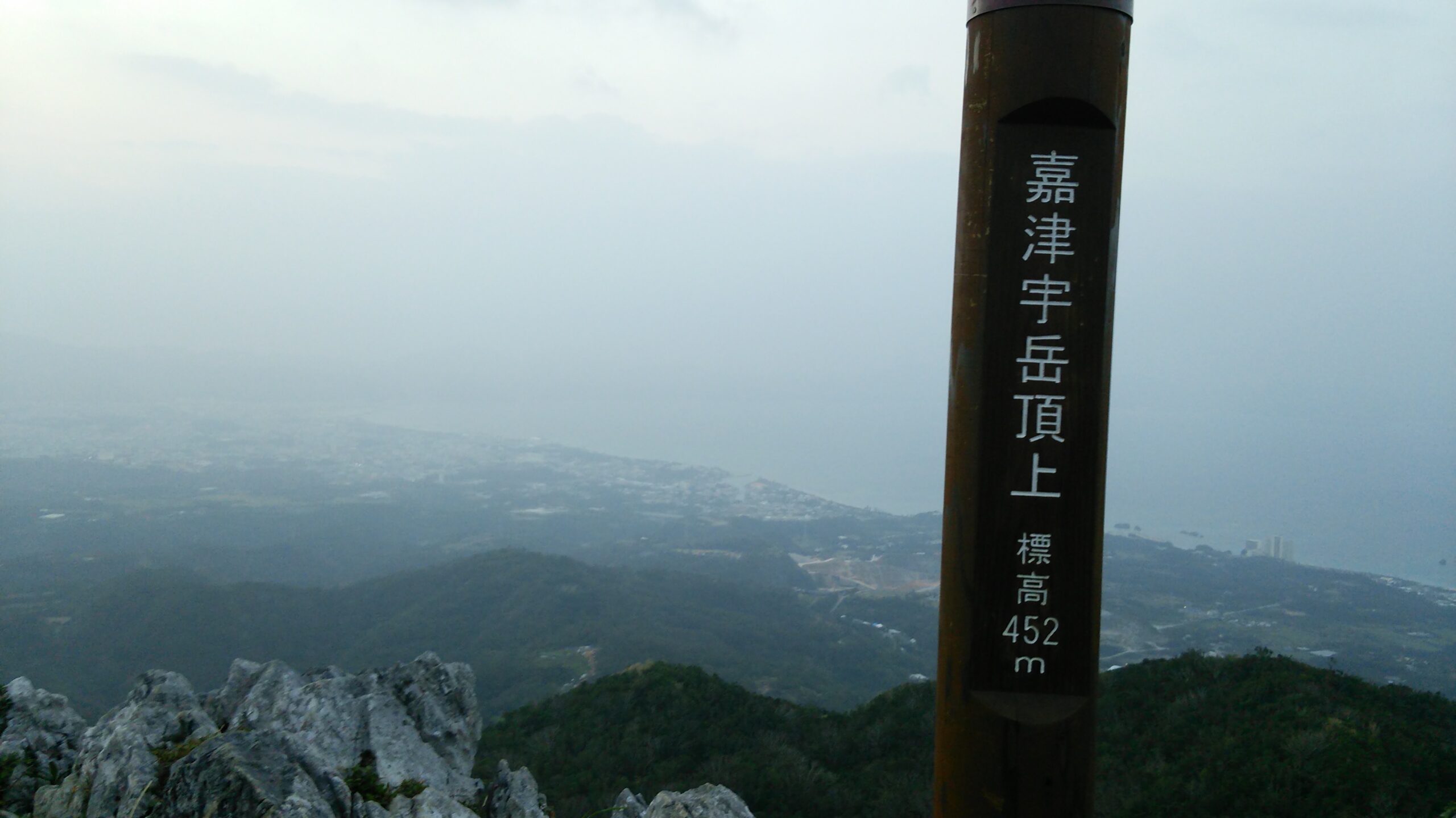 嘉津宇岳の山頂標識(標高452m)と名護の街・海の眺望